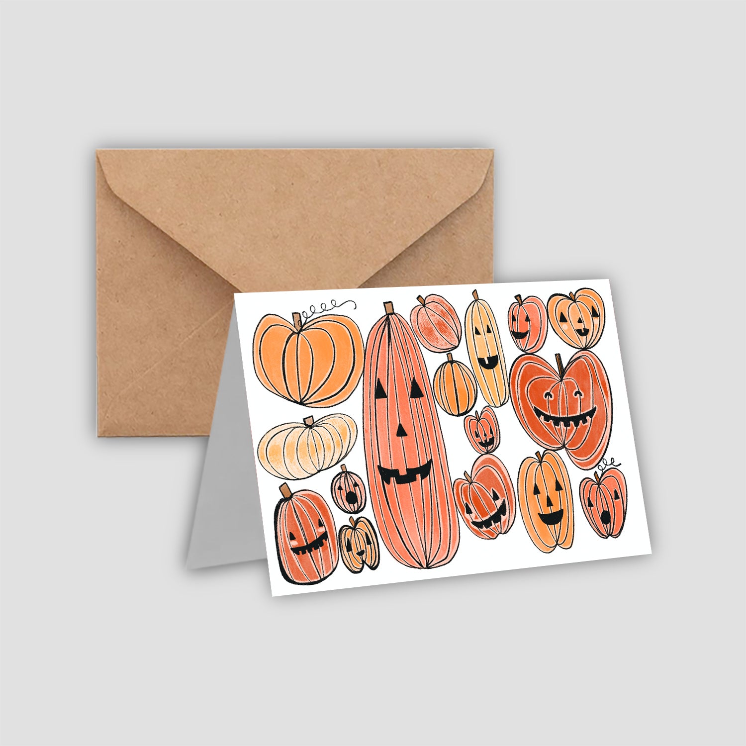 A white greeting card with pumpkins and jackolanterns drawn on the front in a cartoon style. A brown envelope is included.