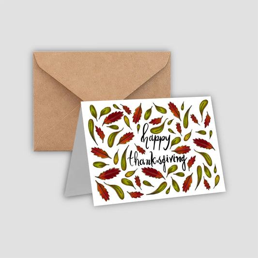 Fall leaves surround the words ‘Happy Thanksgiving’ on a white greeting card with a brown envelope.